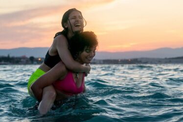 Foto de uma mulher andando na água, carregando outra mulher nas costas
